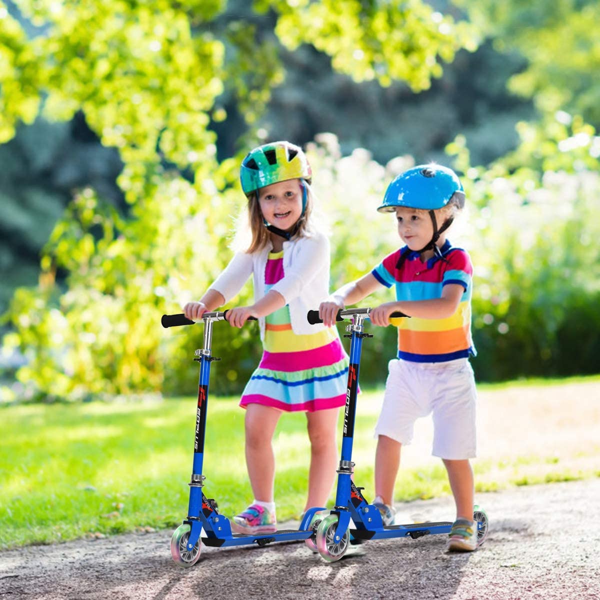 Two children wearing helmets riding the blue stunt scooters in a park