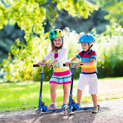 Two children wearing helmets riding the blue stunt scooters in a park