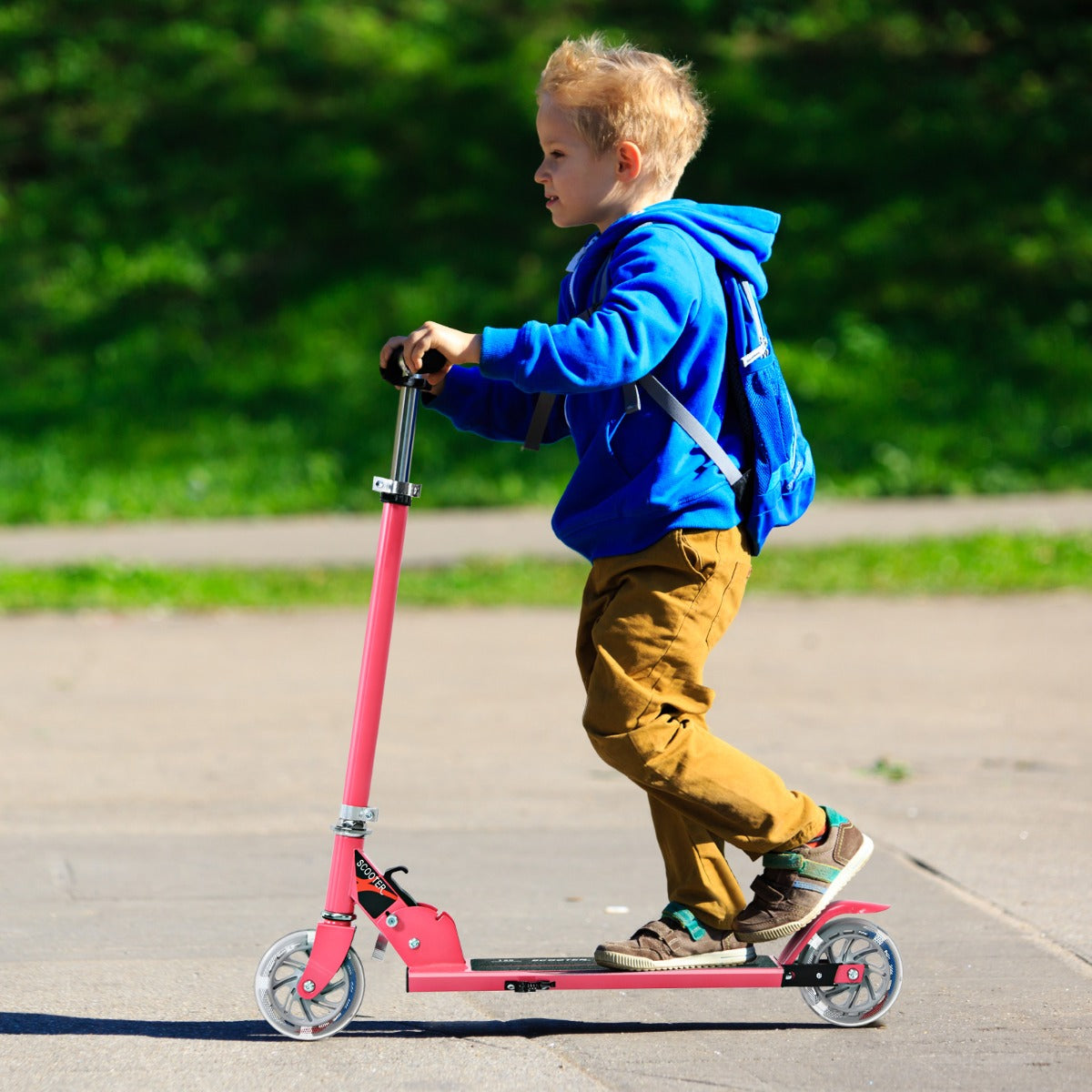 A young boy in a blue hoodie riding the pink stunt scooter on a paved path outdoors