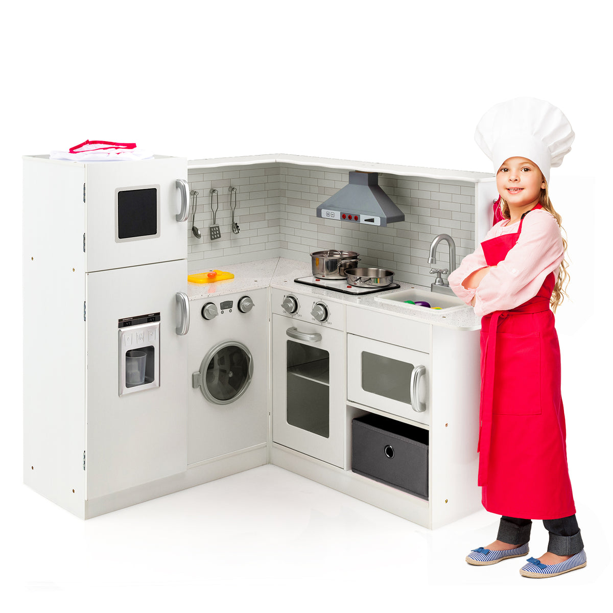 A girl in a chef hat and apron stands next to a white play kitchen set