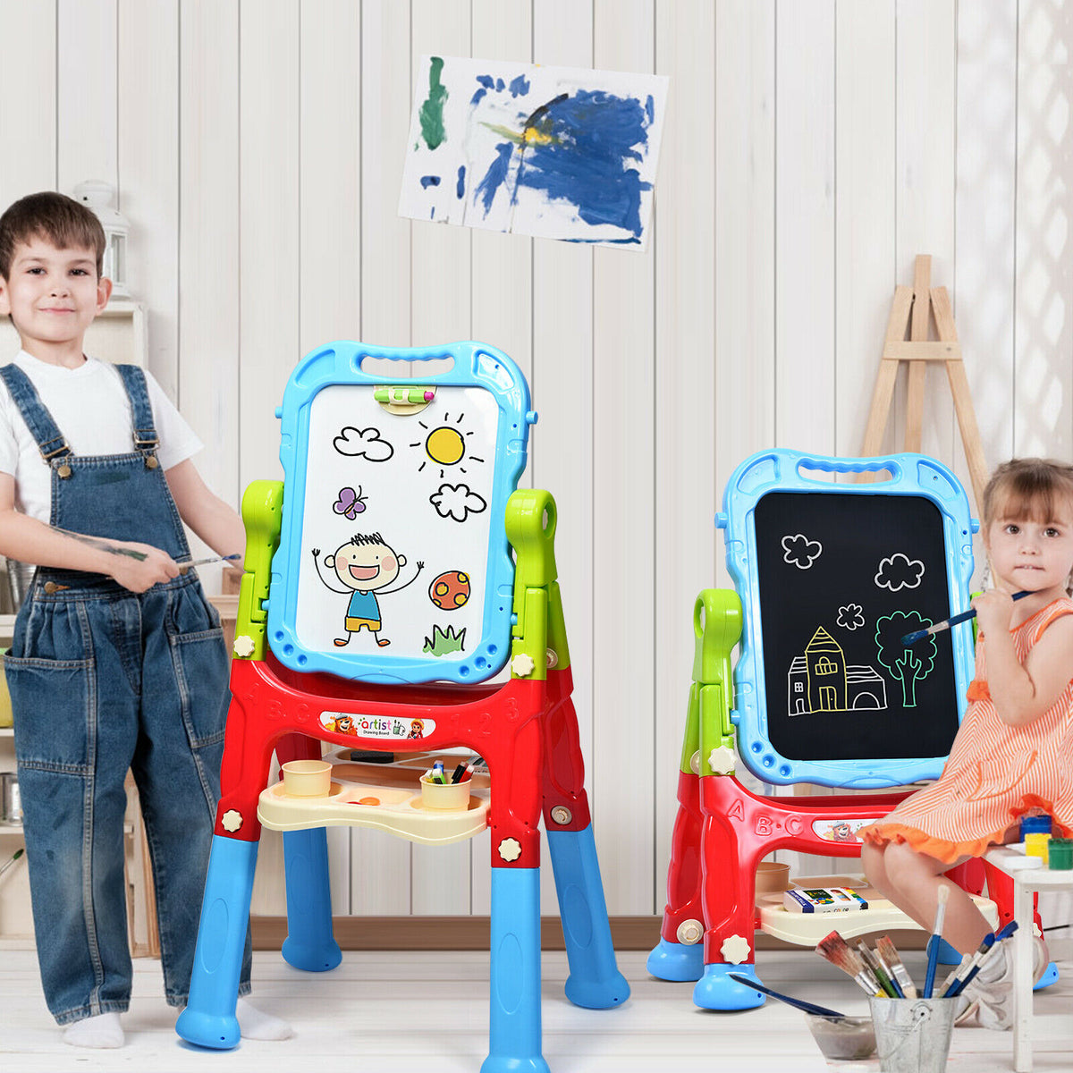 Two children play with the art easels in a room with art supplies around them