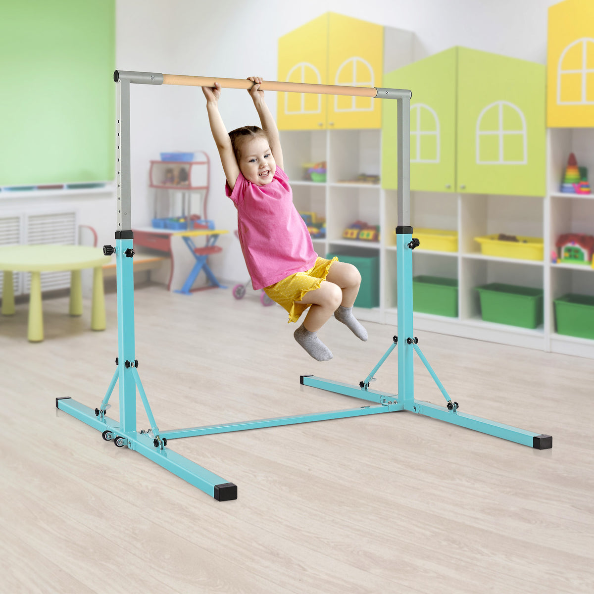 A young girl hanging from the green gymnastics bar in a colourful playroom setting