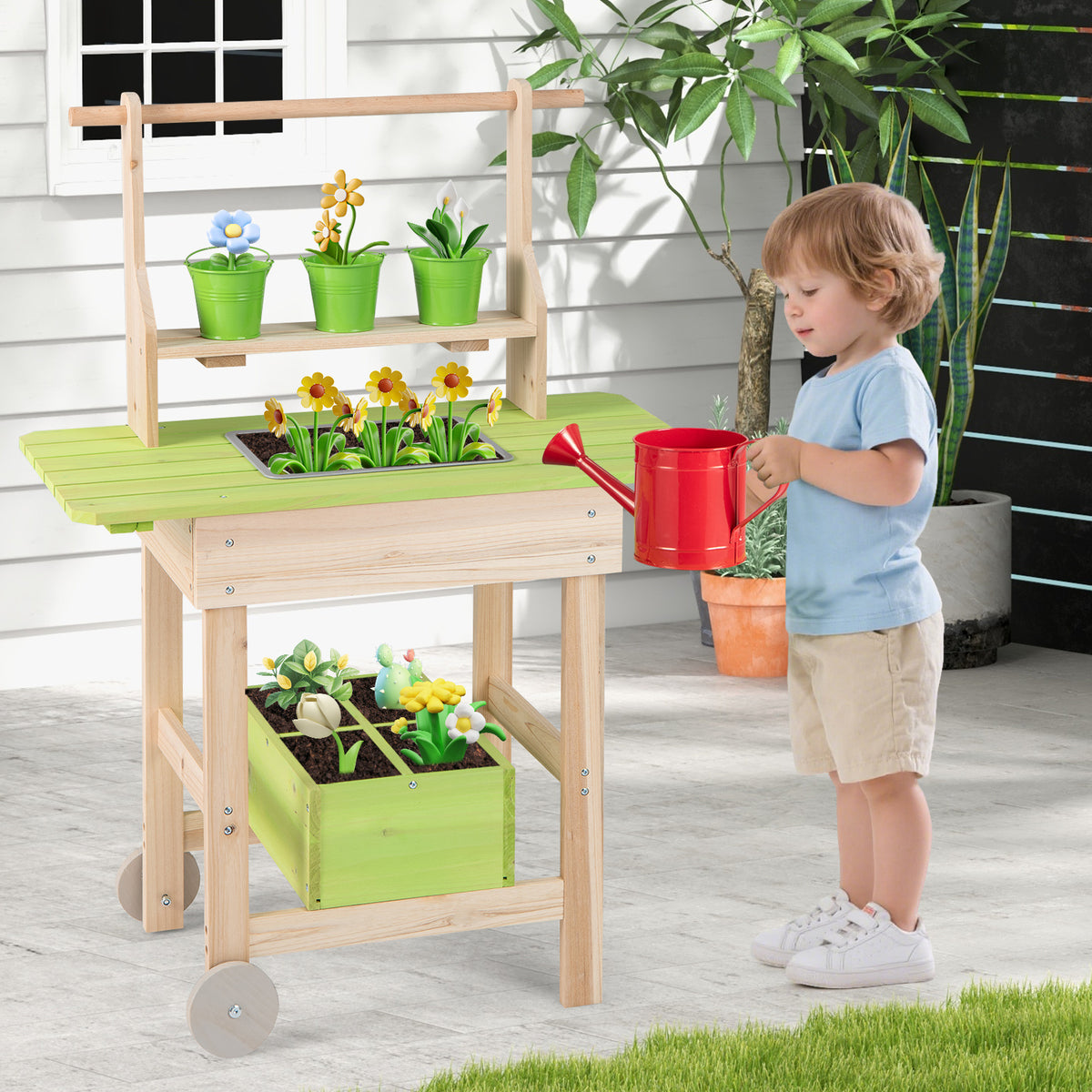 The wooden play kitchen set positioned on a patio with a toddler playing with the red watering can