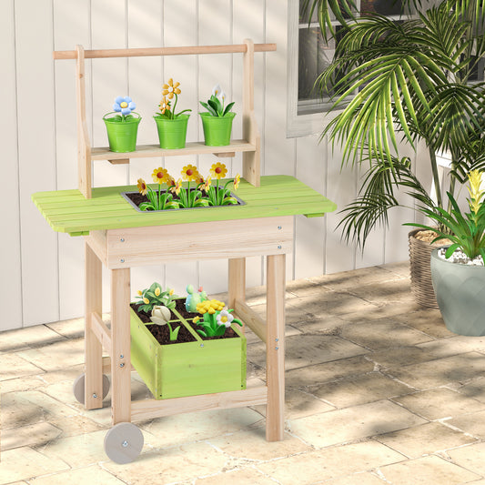 The play kitchen set standing on a paved patio next to a large potted plant in a sunny garden