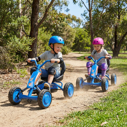 Two children riding the pedal ride on toys along a dirt path in a park with trees