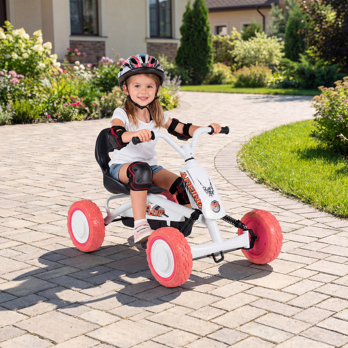 A young girl wearing a helmet rides the white pedal go kart on a paved path outdoors