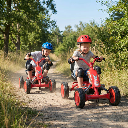 Two children enjoying riding the red pedal go karts on a dirt track