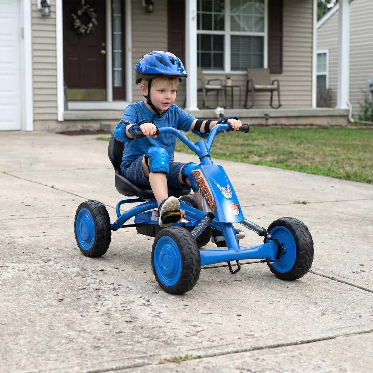 The pedal ride on toy being driven by a young boy on a concrete driveway in front of a house