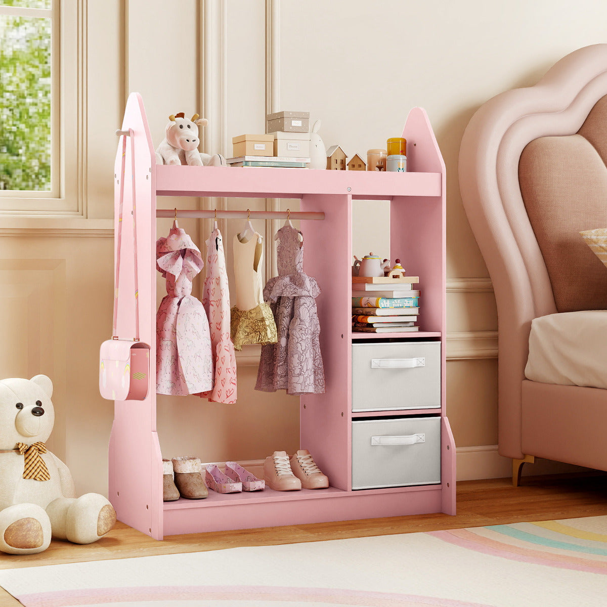 Pink kids play armoire dresser in a bedroom with a large teddy bear and a pink bed