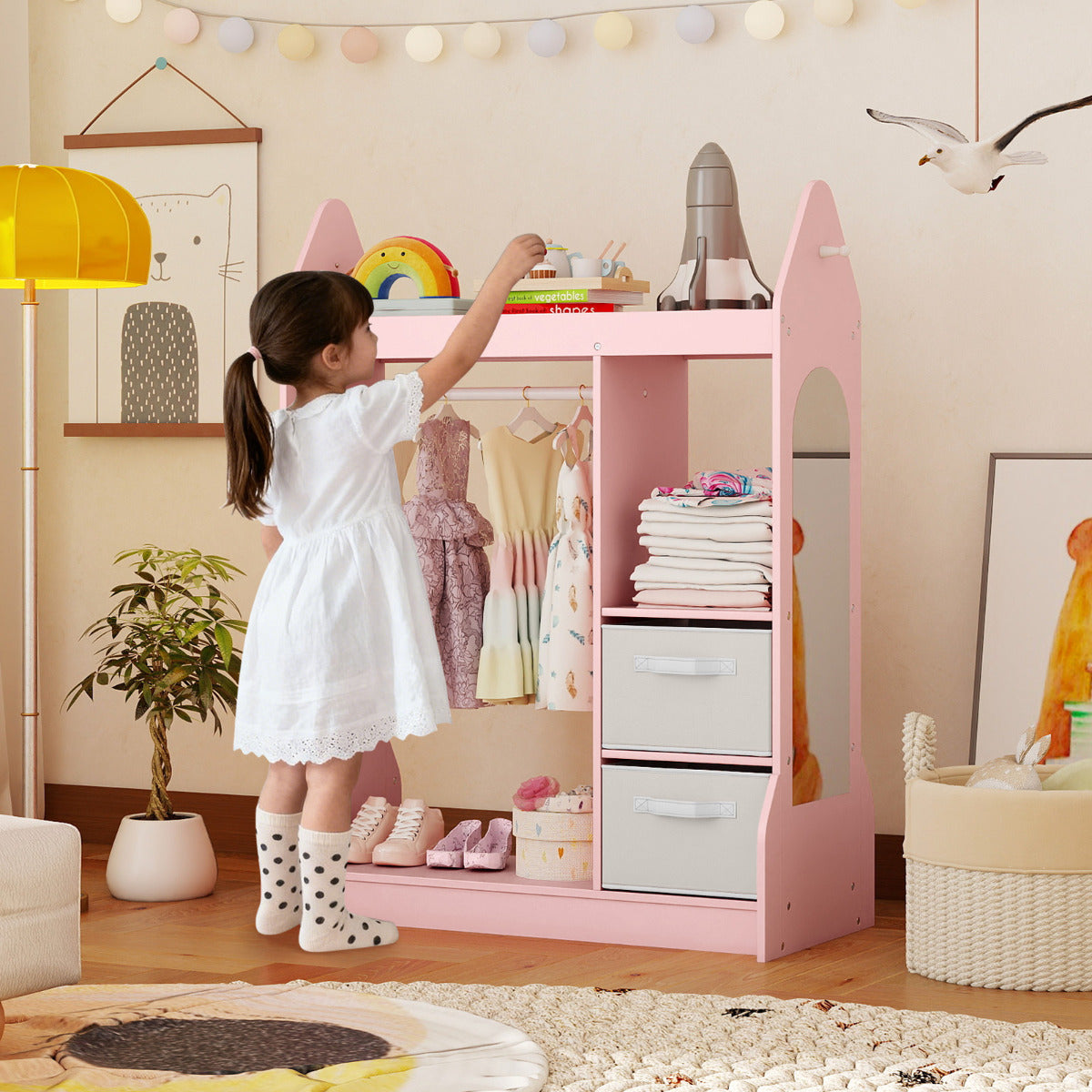Child reaching for toys on the top shelf of the pink kids play armoire dresser