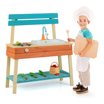 A boy in a chef's hat holding a wooden spoon and cutting board next to the play kitchen