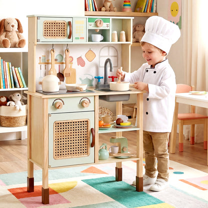 A young boy wearing a chef's hat plays with the green wooden pretend kitchen
