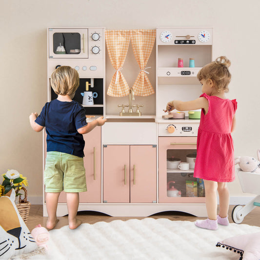 Two children playing with the pink wooden play kitchen set, one at the stove and one at the microwave
