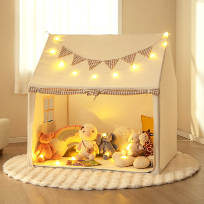 The play tent illuminated by fairy lights, placed on a round rug with various plush toys