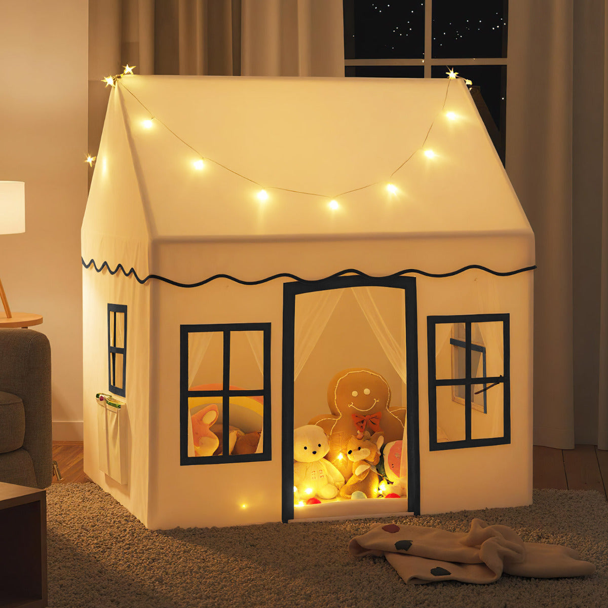 The beige play tent is lit up with fairy lights and filled with toys and stuffed animals