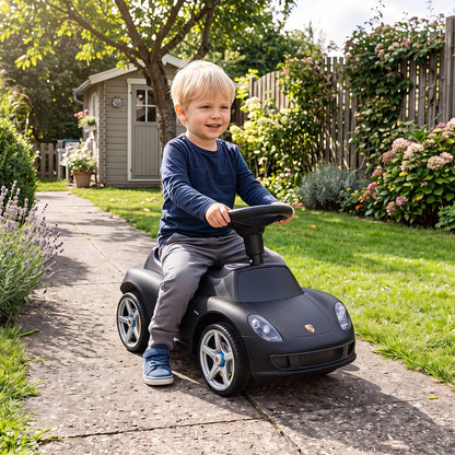 A young boy enjoys riding the black Porsche style sliding car in a garden setting