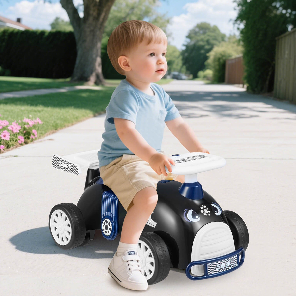 Toddler boy sitting on the black and blue sliding toy car outdoors on a paved path