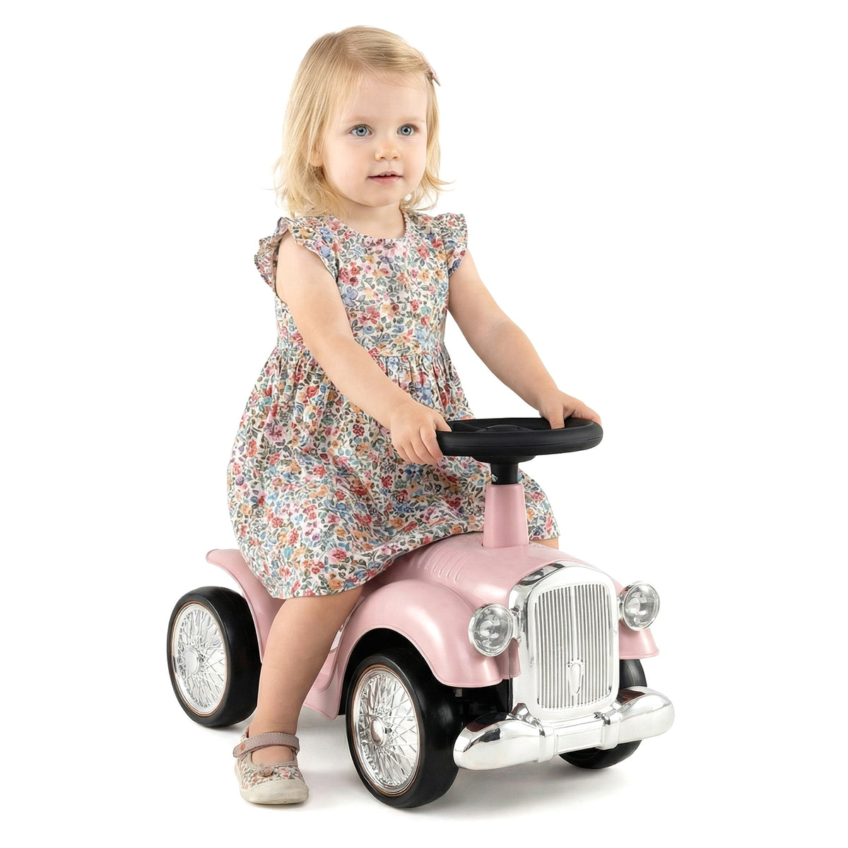 A little girl sits on the pink push and pedal ride on toy