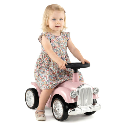 A little girl sits on the pink push and pedal ride on toy