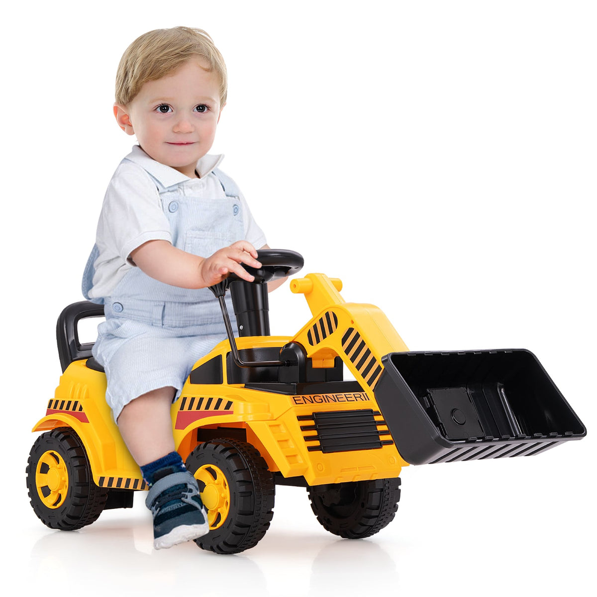 A toddler sits on the yellow ride on digger toy with a black steering wheel and front loader