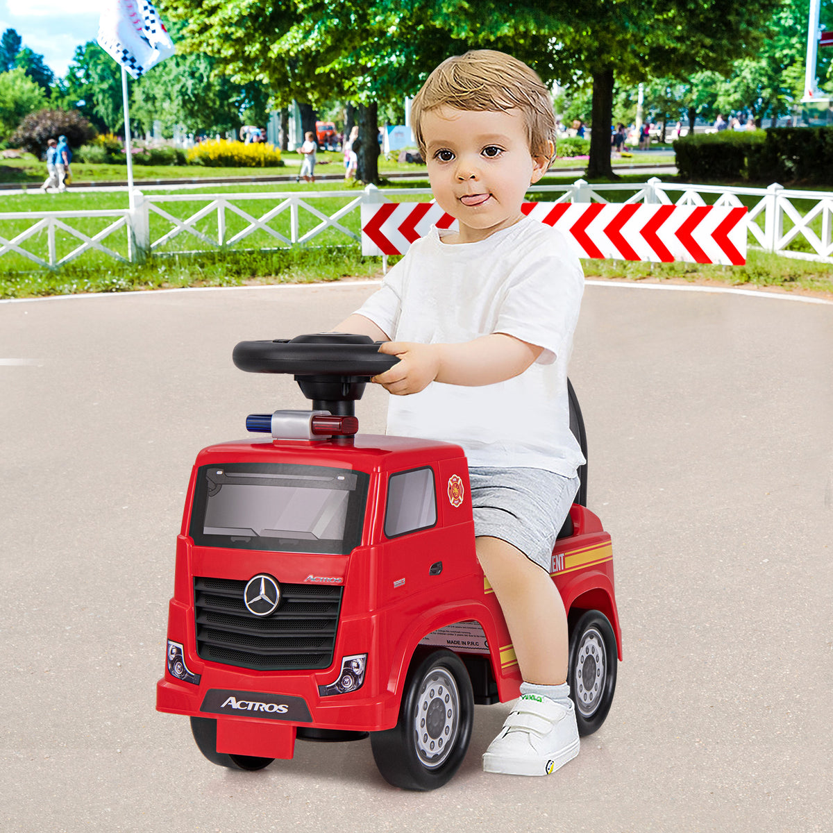 A young boy happily rides the red fire truck toy on a paved path outdoors