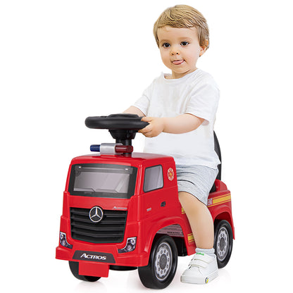 A toddler sits on the red fire truck toy, steering with the wheel