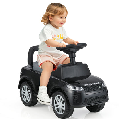 A happy toddler steers the black ride on push car while sitting on the seat