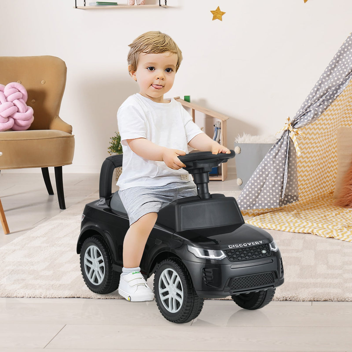 A toddler sits on the black foot-to-floor walking sliding toy car, steering it indoors