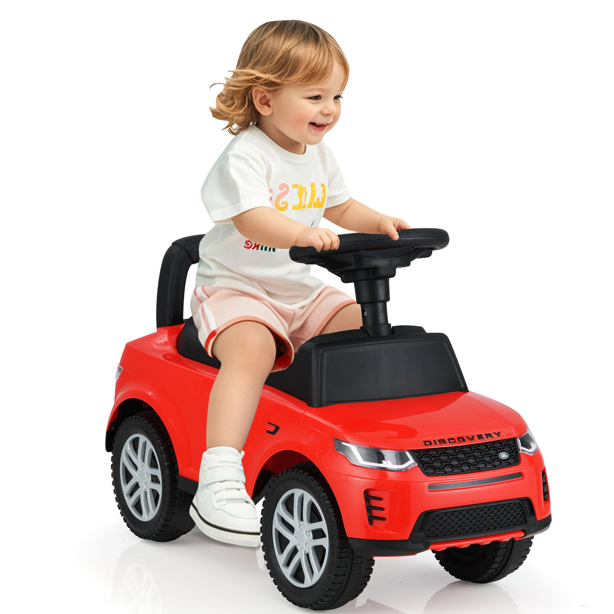 A smiling toddler sits on the red ride on push car, looking forward