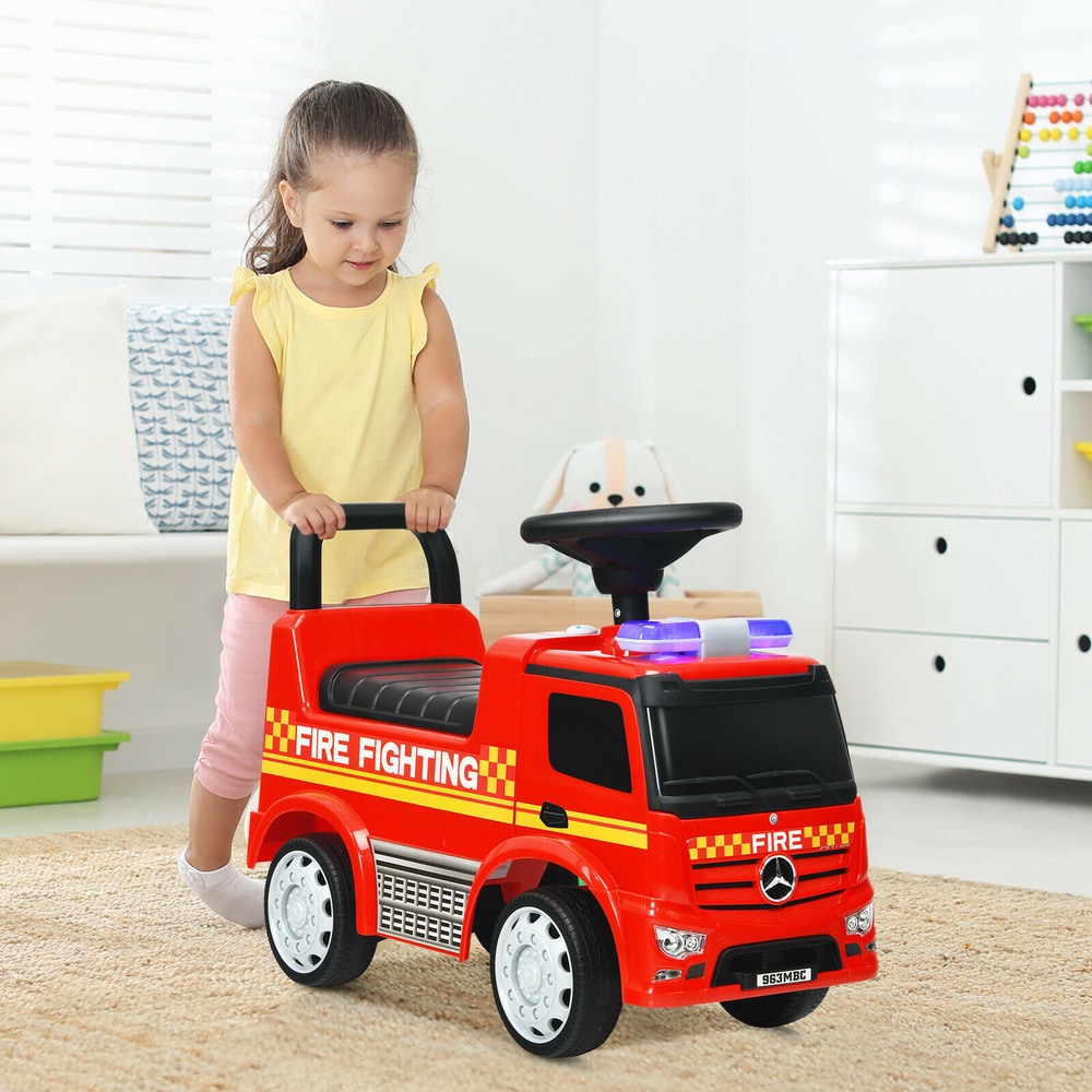 A young girl pushing a red Mercedes Benz firefighter ride on car indoors