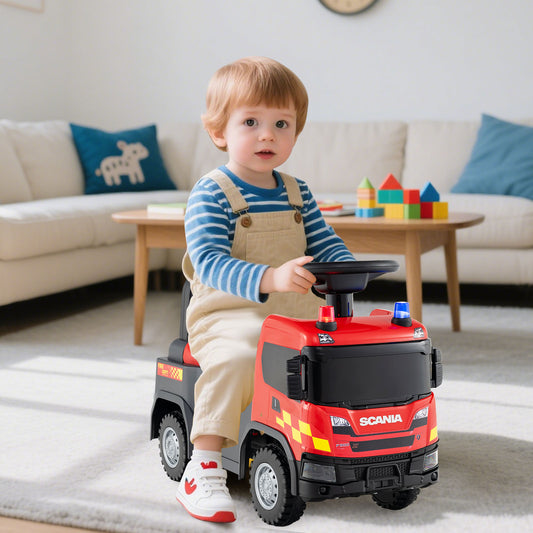 A young boy in overalls sits on the red push car in a living room setting