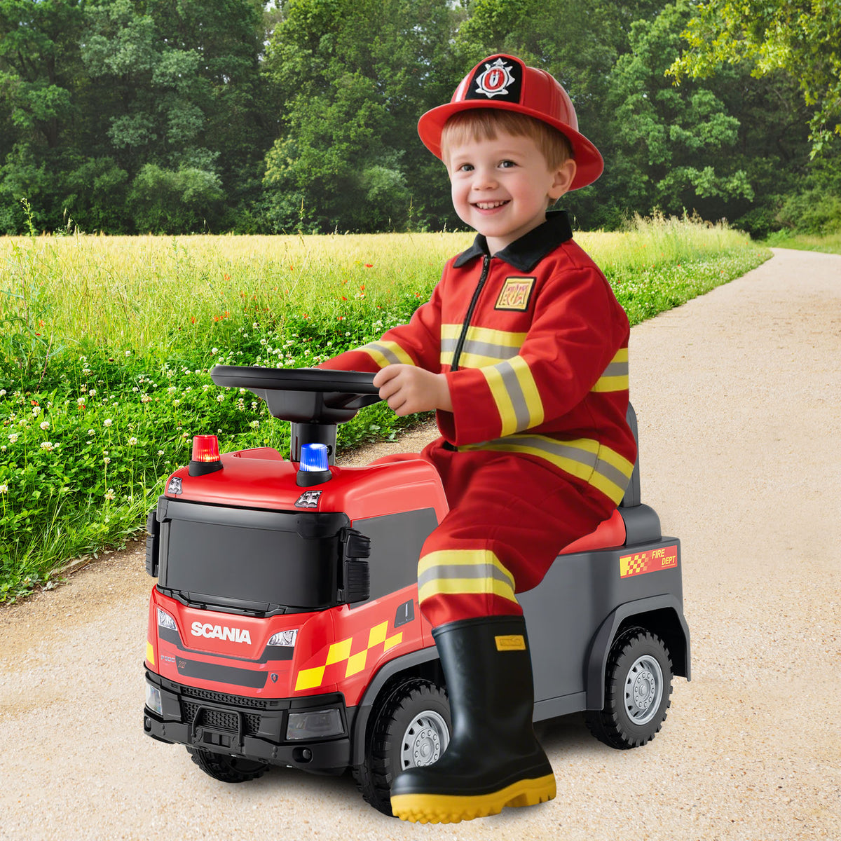 A smiling boy in a firefighter costume rides the red push car outdoors on a path