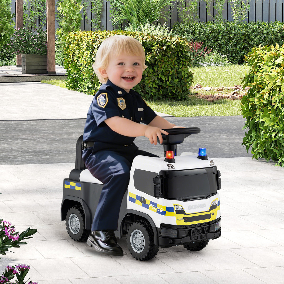 A happy toddler in a police uniform sits on the push and pedal ride on toy in a garden