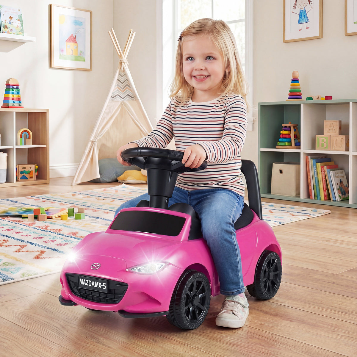 A happy toddler sits on the pink Mazda ride on toy in a playroom