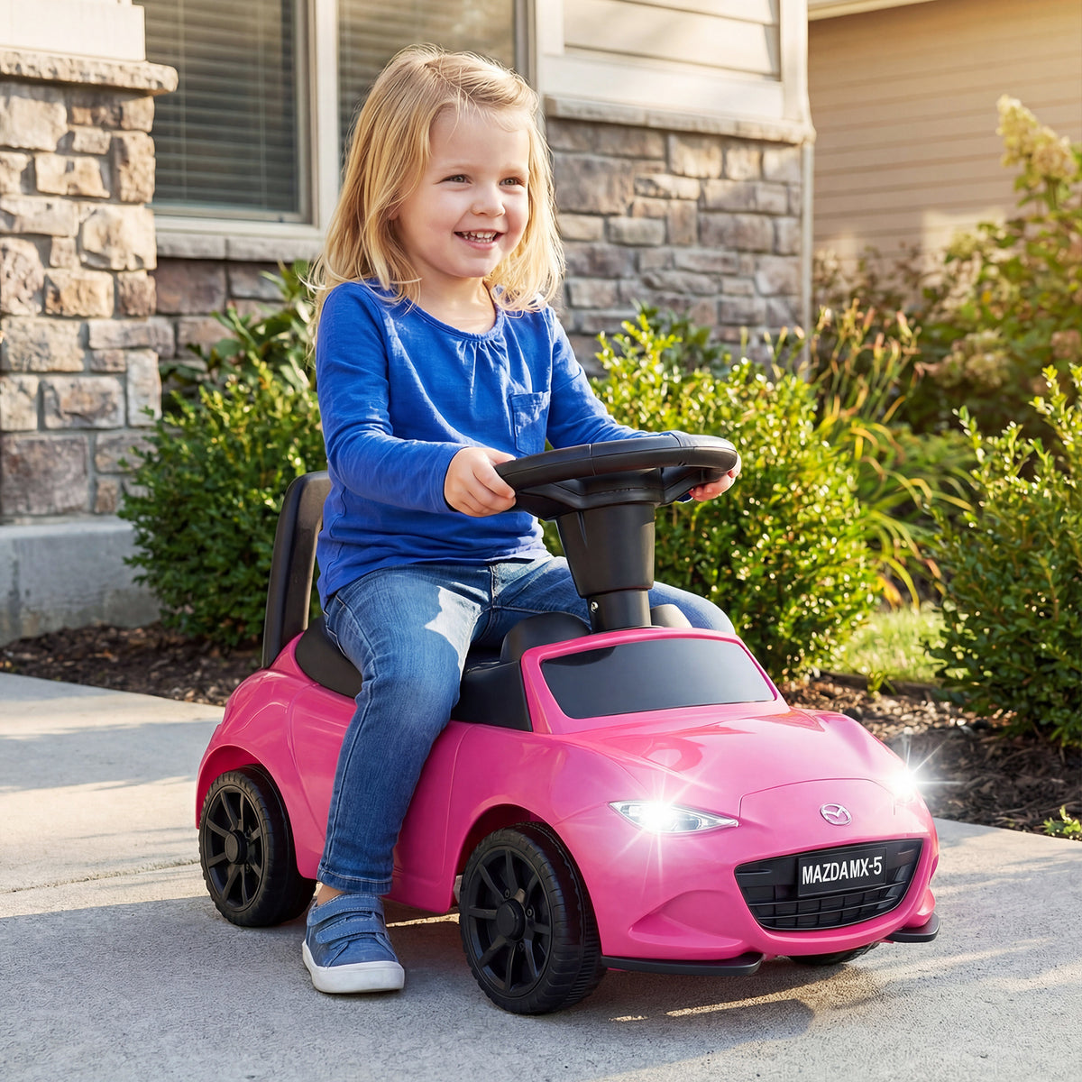 A child rides the pink Mazda sliding toy on a paved path outside