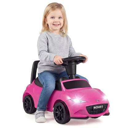 A young girl enjoys riding the pink Mazda toy car indoors
