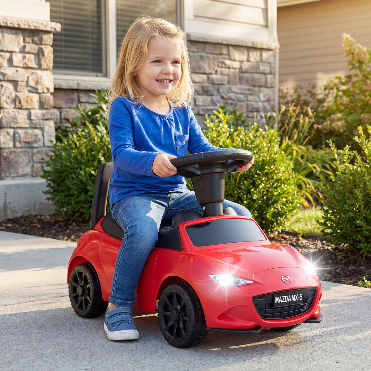 The ride on toy being driven by a child on a paved driveway outside a house