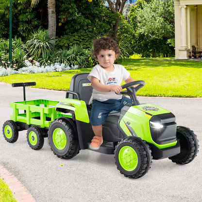 A toddler sits on the green electric tractor with trailer, steering it