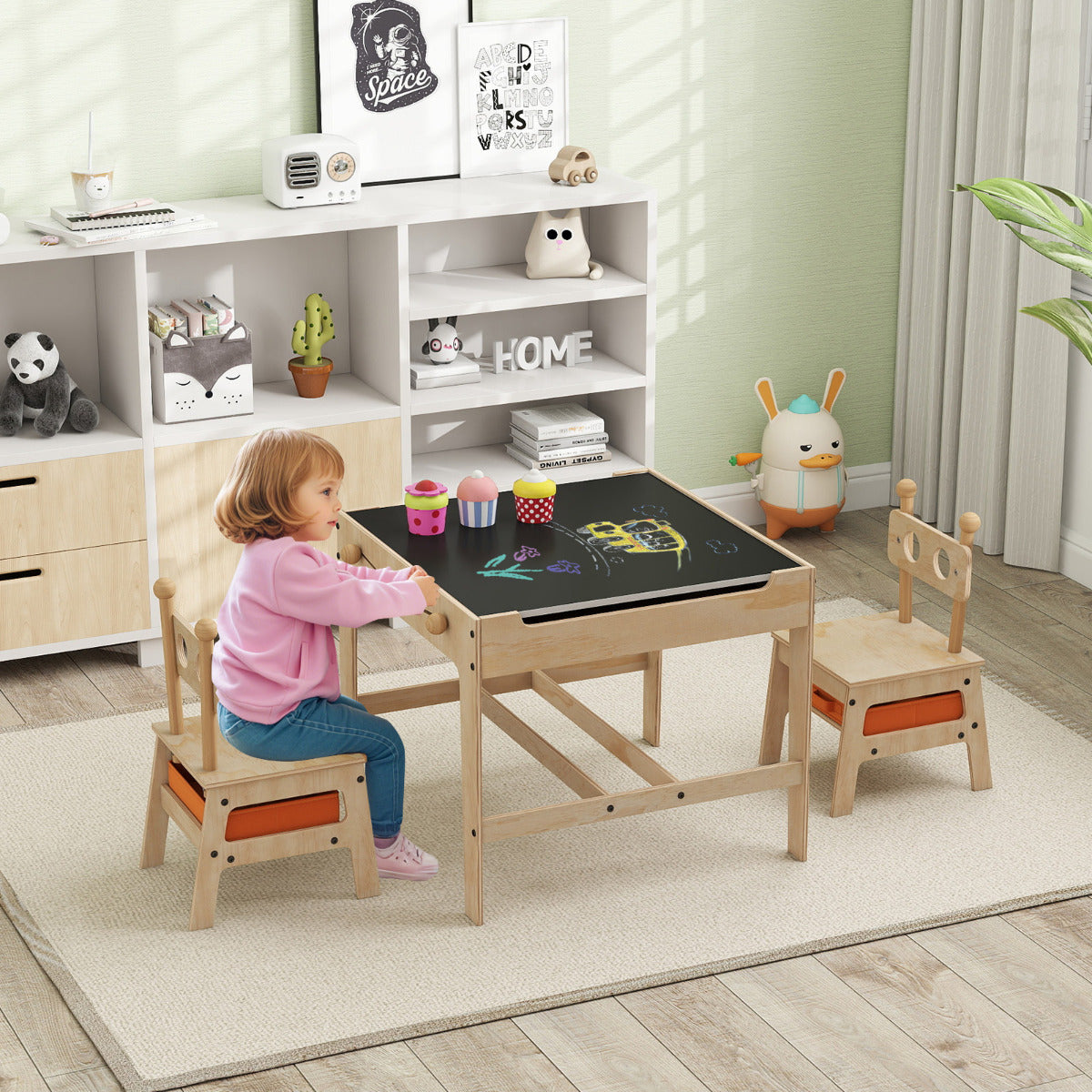 A young girl sits at the activity desk, drawing on the blackboard surface with chalk