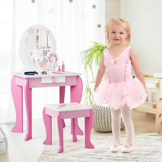 A young girl in a pink ballet outfit stands next to the pink vanity table and chair set