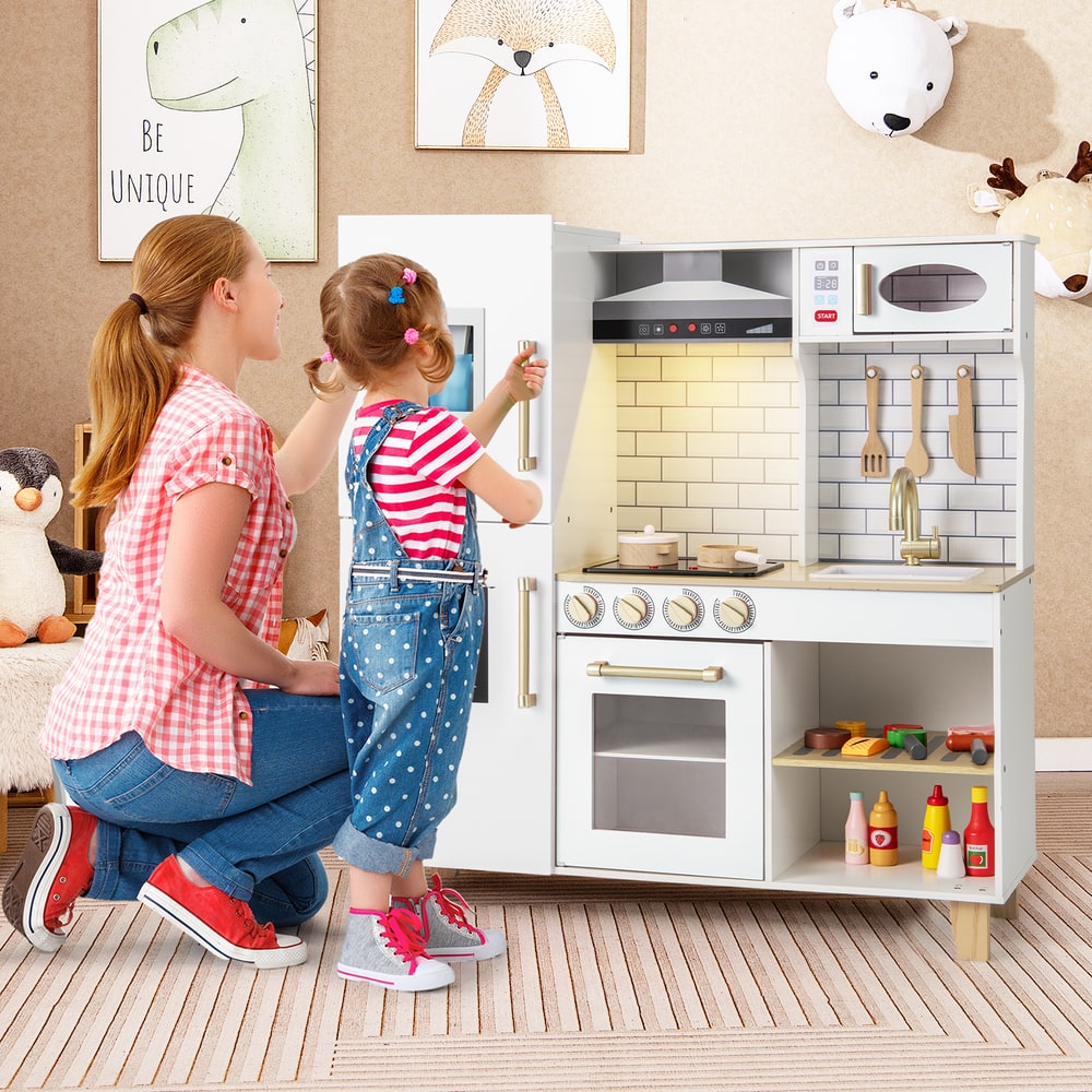 A mother and child playing with the white play kitchen set