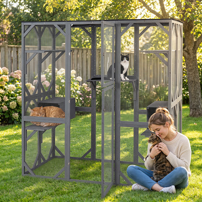 A woman sits in a garden holding a cat next to the outdoor cat enclosure