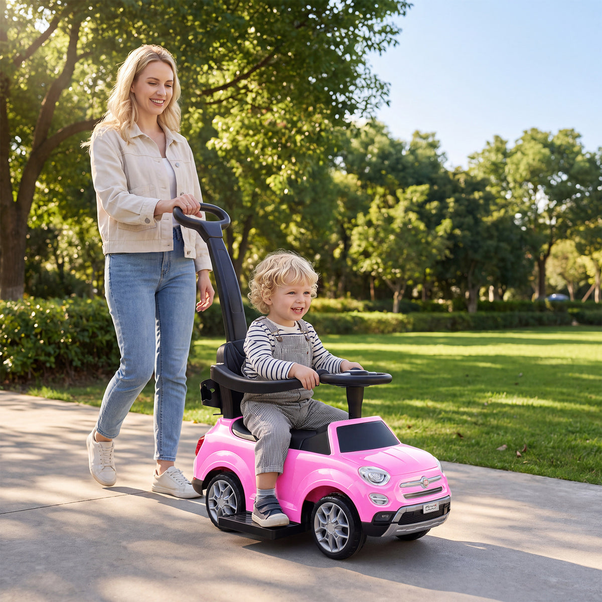 A woman pushes a toddler sitting in the pink push & pedal ride on toy down a path