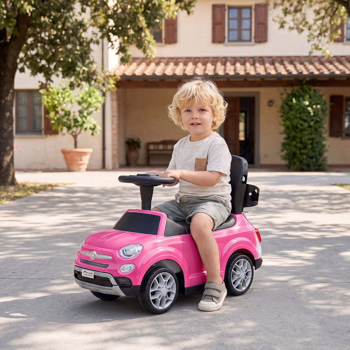 A young boy sits and steers the pink push & pedal ride on toy outside a house