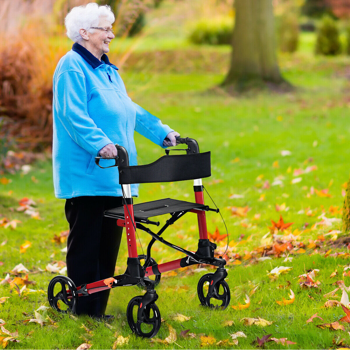 An elderly woman smiling while using the red mobility aid to walk across a grassy park in autumn
