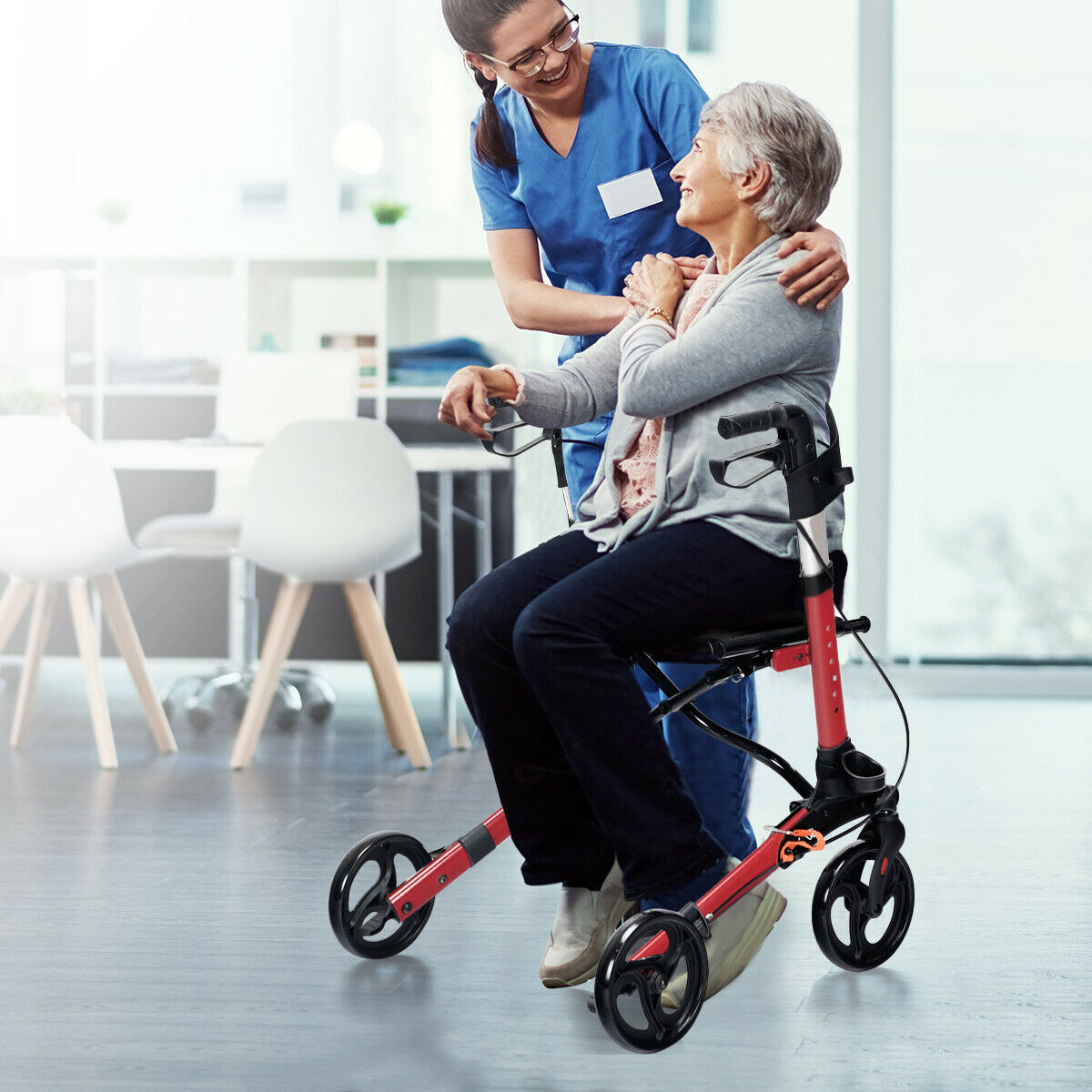A woman sitting on the seat of the red mobility aid while being assisted by a healthcare worker