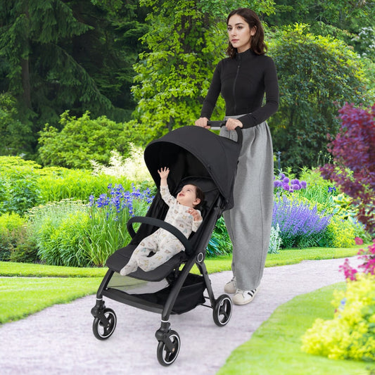 Woman pushing the black baby stroller with a baby inside, on a paved path in a park