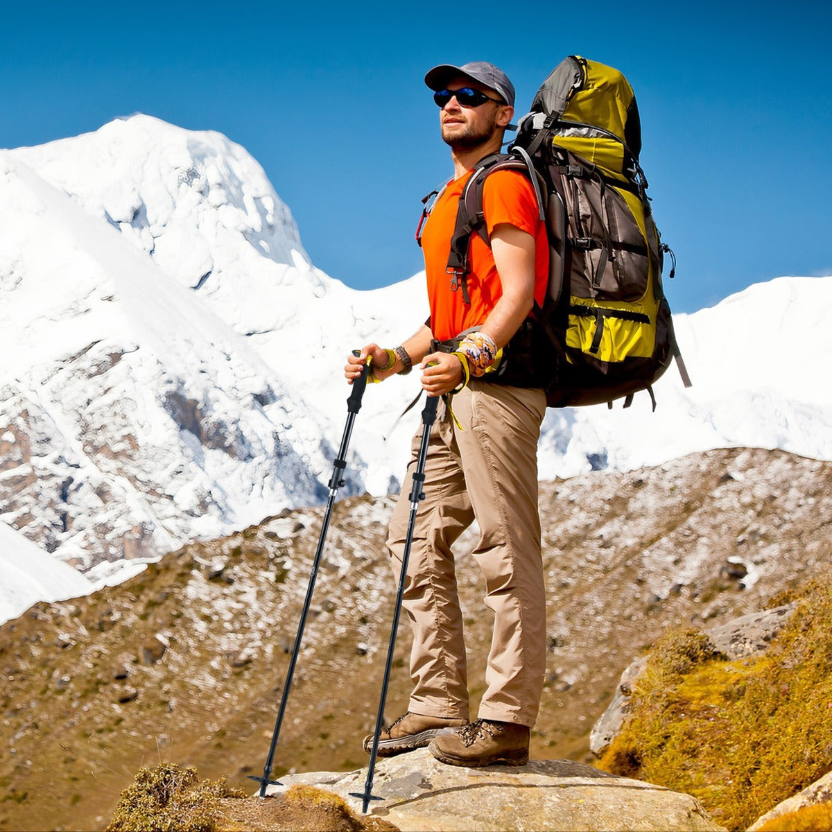 The yellow camping poles are used by a man standing on a rock in a mountainous landscape