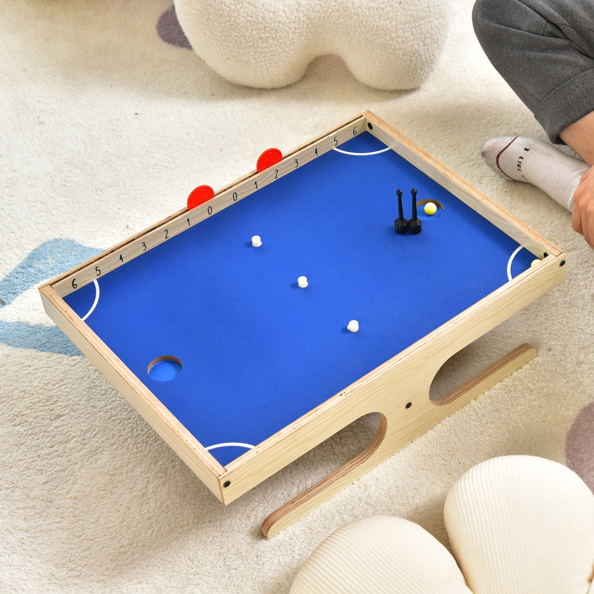 The magnetic mini foosball table on a rug with a person's legs visible