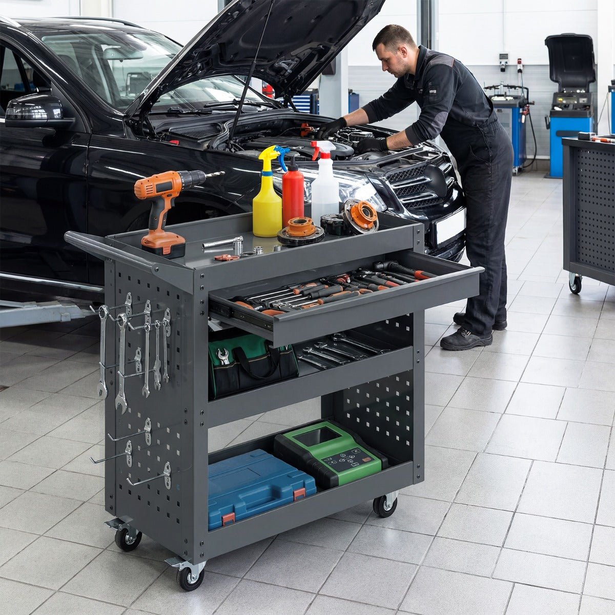 Mechanic using the grey tool organizer trolley next to a car